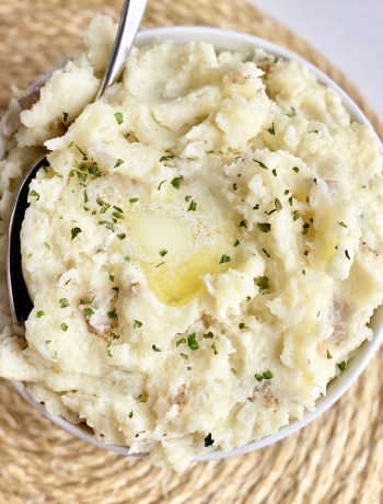 Bowl of garlic mashed potatoes with butter on top and parsley.